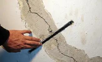 A wall with a large crack is being inspected by a professional in Marietta, GA